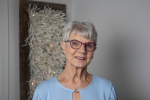 Seniorinainen katsoo hymyillen kameraan.